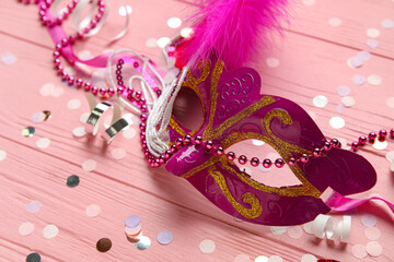 Beautiful carnival mask with confetti and beads on pink wooden background
