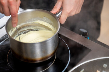 A hand stirs a creamy mixture in a stainless steel saucepan on an induction cooktop, highlighting the preparation of sauce or custard.