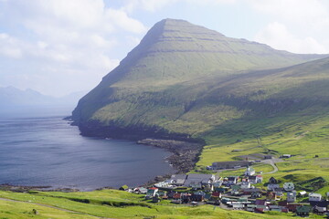 The steep cliffs and beautiful green valley of Gjogv by the blue Atlantic Ocean in Faroe Islands
