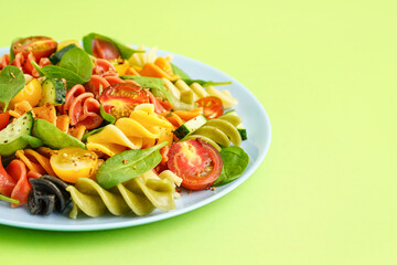 Plate with Italian pasta salad on green background