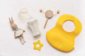 Feeding bottle with milk for baby, toys, teether and bib on light background