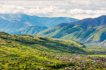 Obraz premium mountainous countryside landscape with kolochava village in the valley. cloudy weather. rural fields and meadows on the forested slopes of a hill. rolling alpine scenery in spring