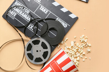 Movie clapper with popcorn and film reels on beige background