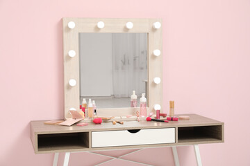 Dressing table with different decorative cosmetics and makeup accessories near pink wall