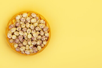 Top view of wicker basket full of painted small easter eggs on vibrant yellow table with copy space