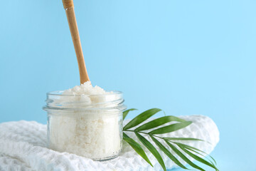 Glass jar with natural body scrub, clean towel and palm leaf on color background