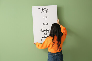 Young woman hanging poster on green wall at home