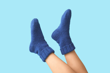 Legs of young woman in blue knitted socks on color background
