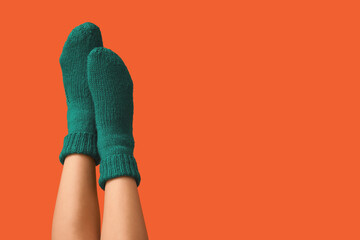 Legs of young woman in green knitted socks on orange background