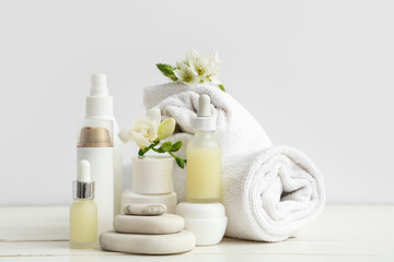 Composition with cosmetic products, spa stones, clean towels and flowers on light wooden table
