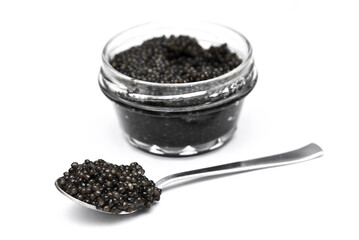 Black caviar close up view in heap spoon and glass jar on white background.