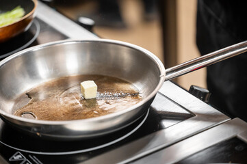 Close-up of a stainless steel frying pan on a stovetop, featuring a cube of butter melting inside. Ideal for concepts of cooking, food preparation, and culinary simplicity.