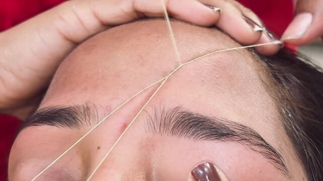 close up of a young woman shaping eyebrows and doing forehead with thread art.