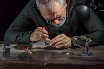 Watchmaker repairing watches looking through magnifying glass monocular. Professional senior watch fixer in repair services workshop.