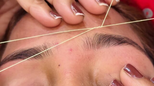 Close-up of a eyebrows, woman's hands doing threading.