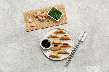 Plate of fried Japanese gyoza with bowl of soy sauce and seaweed salad on grey background