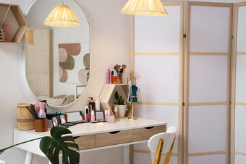 Interior of light dressing room with makeup table, mirror and folding screen