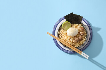 Bowl of tasty Chinese noodles with boiled egg, mushrooms and seaweed sheets on color background