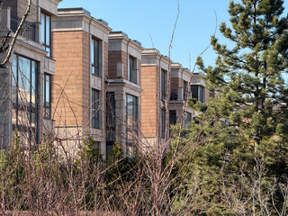 modern, multi-story residential buildings with large windows and beige stone facades. The architecture is elegant and contemporary. The weather is clear and sunny, with a bright blue sky