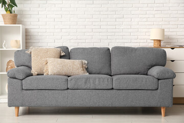 Interior of stylish living room with comfortable sofa, dresser and shelving unit near white brick...