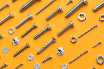 Arrangement of different tap bolts, screws and chrome nuts on orange background