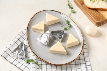 Plate with triangles of tasty processed cheese, micro green and napkin on light background