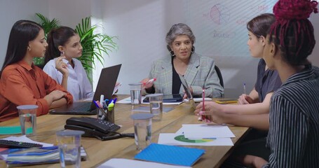 Indian young adult woman team sitting old aged boss ceo lady leader use tablet show growth chart at job place girl staff group study stock data work check new graph share day plan ideas office room - Powered by Adobe