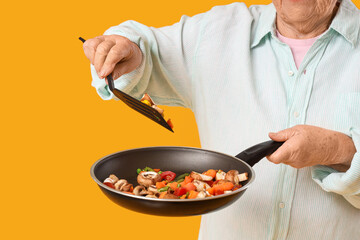 Senior woman with fried vegetables on yellow background, closeup