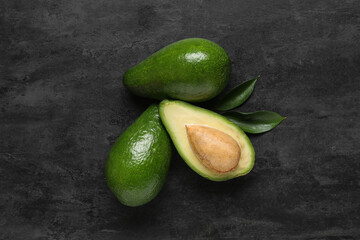 Fresh ripe avocados and leaves on black background