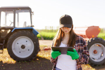 a girl agronomist with a tablet manages agribusiness against the background of a tractor, modern agribusiness