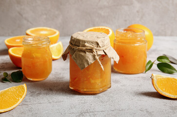 Jars of sweet orange jam and fruits on grey background