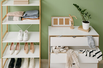 Interior of messy living room with shelving unit and scattered clothes in commode near green wall