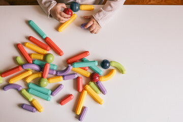 Children playing with colorful magnetic building toys on a white table. Educational and creative play concept with kids' hands arranging various shaped pieces