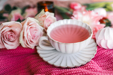 Elegant ceramic cup with pink tea on a matching saucer, surrounded by fresh tulips, roses, and cozy textures. Feminine flat lay with soft pastel tones and romantic spring vibes