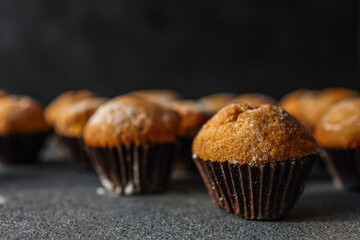 Freshly baked golden muffins in dark paper liners arranged on a textured surface, with shallow...