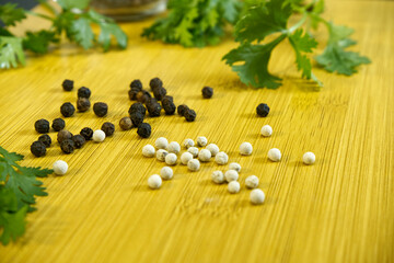 Pepper on wooden board around with blurred coriander leaves. Close-up black and white peppers. Herbal, ingredient, cooking, favor, food, herb, vegetable and rustic kitchen concepts. Still-life food.
