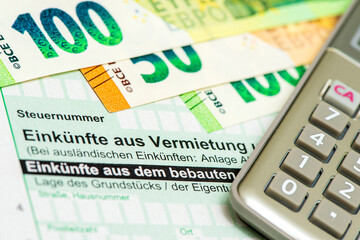 Ein Taschenrechner und Euro Geldscheine liegen auf einem Formular für die Steuererklärung an das...