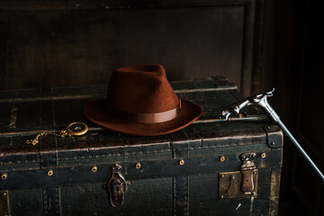 Classic adventure elements with a felt hat, cane, and pocket watch on an antique trunk, evoking nostalgia and exploration.