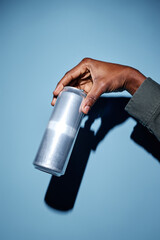 Hand holding metallic can with shadow casting against blue backdrop, showing minimalistic style...