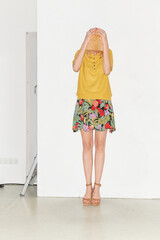 modisch gekleidete junge blonde Frau mit buntem Rock, Polohemd und Hut vor weisser Wand im...