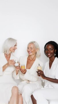 Three women showcasing skincare products while dressed in white against a neutral backdrop in a beauty studio. Ideal for Social Media, Stories, Advertising