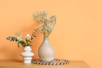 Flowers in vases on table near orange wall in room. Closeup
