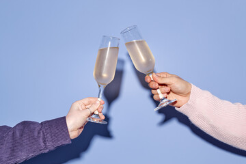 Two hands clinking champagne glasses in joyful celebration against a blue backdrop. Clear bubbles...