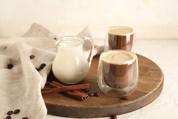 Glasses of hot coffee with cinnamon and jug of fresh milk on white background