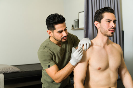 Latin man receiving dry needle treatment on shoulder from professional physiotherapist during physical therapy session