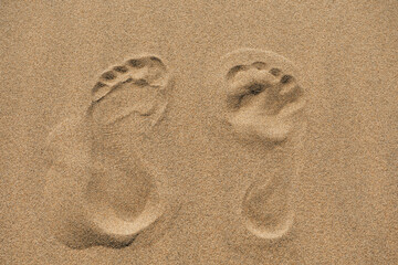 Footprints of bare feet in the dry sand, close up, top down view
