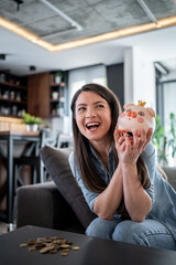 Happy woman saving money holding piggy bank at home