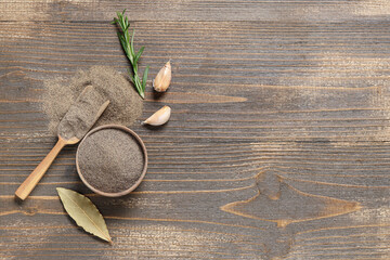 Bowl of black pepper powder with bay leaf, garlic and rosemary on wooden background