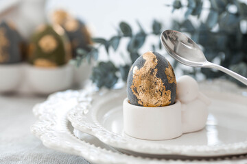 The banner. Table setting. An egg stand with a rabbit, Easter eggs with gilding and a branch of eucalyptus on a linen tablecloth. The concept of a bright Easter holiday.