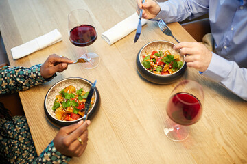 High angle view of multiethnic couple eating salad and drinking red wine at table in the restaurant
